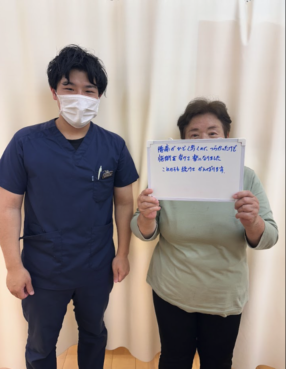 K様直筆メッセージ「腰痛がひどく寝るのがつらかったけど施術を受けて楽になりました これからも続けてがんばります」と担当者と一緒の写真